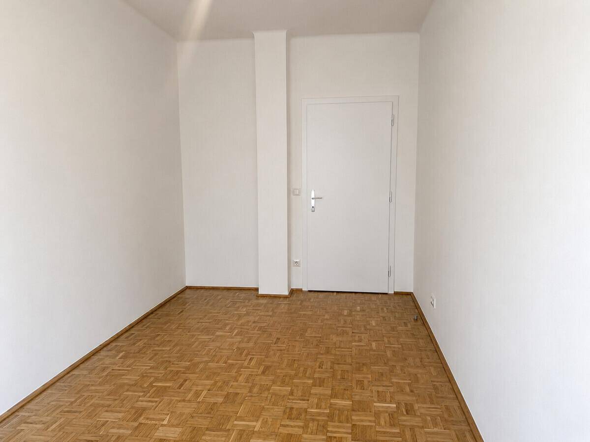 Helles Zimmer mit Parkettboden und weißer Tür, bietet flexible Nutzungsmöglichkeiten.