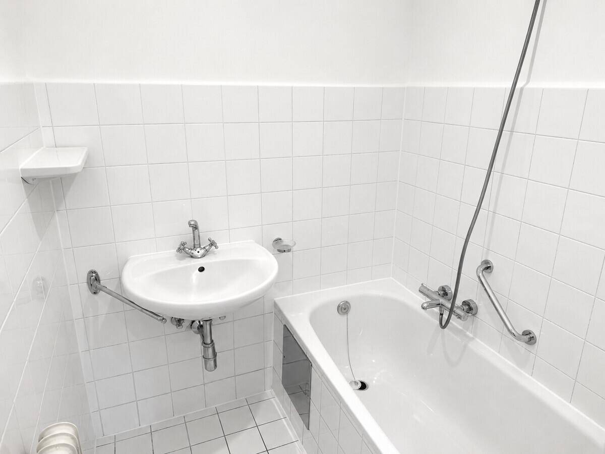 Funktionales Badezimmer mit weißen Fliesen, Waschbecken, Badewanne und Haltegriffen.