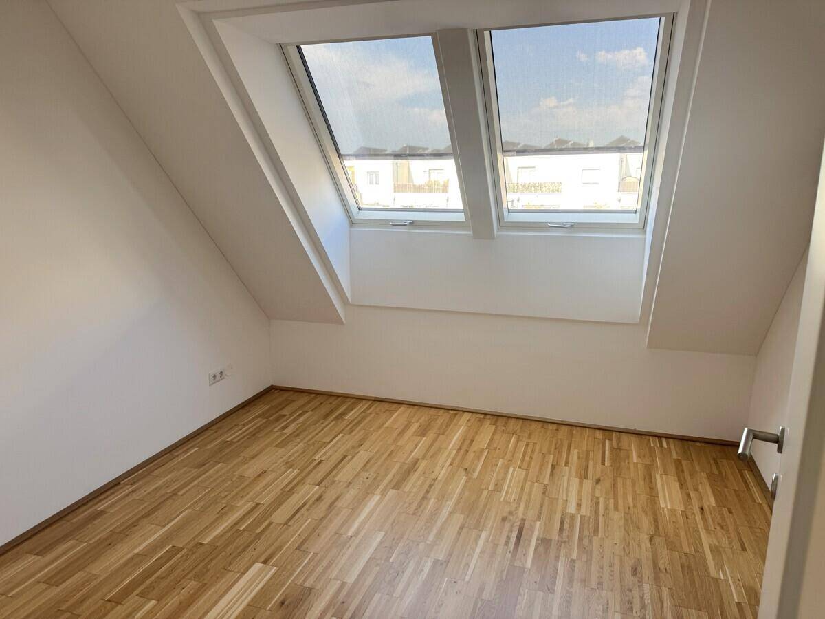 Lichtdurchflutetes Zimmer im Dachgeschoss mit Parkett und zwei schrägen Dachfenstern.