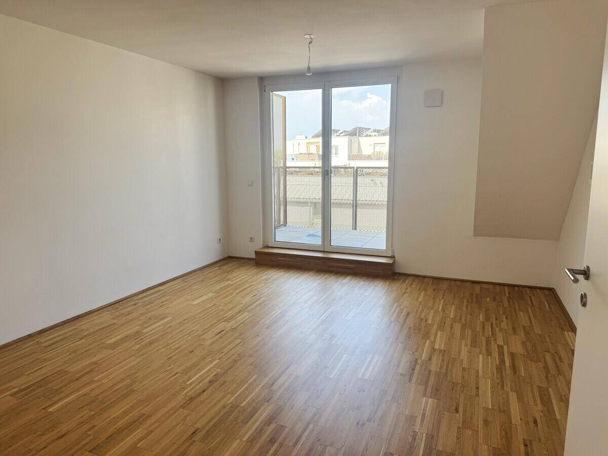 Heller, leerer Raum mit Parkettboden und Zugang zu einem Balkon, ideal als Wohnzimmer.