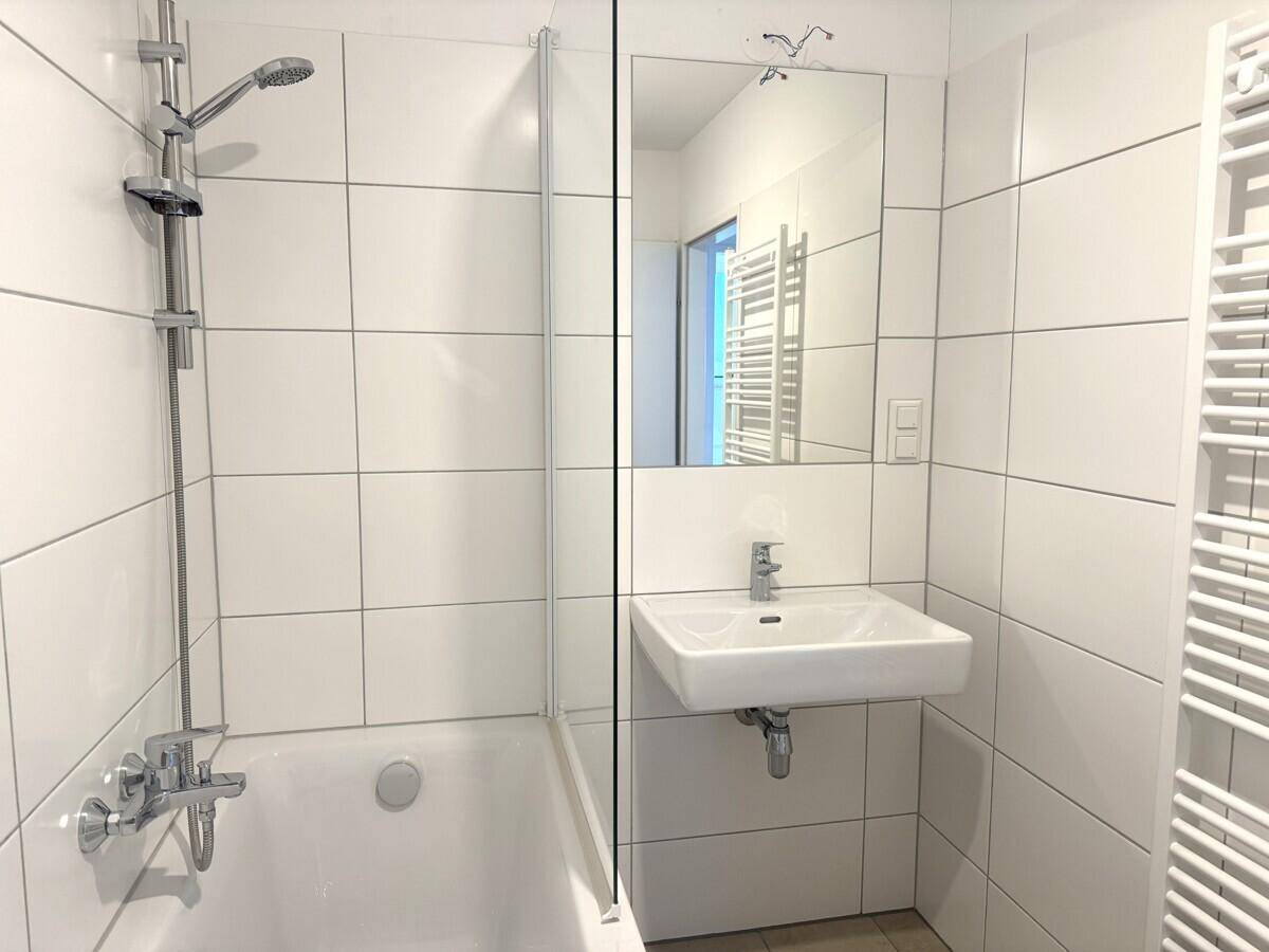Modernes Badezimmer mit weißen Fliesen, Badewanne mit Duschfunktion und Handtuchheizkörper.
