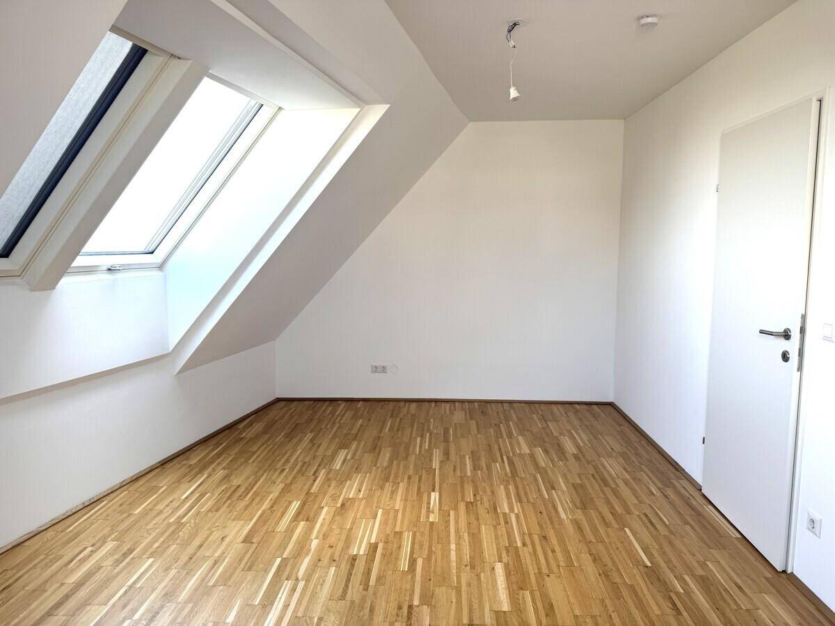 Geräumiges Dachzimmer mit Holzboden und einem großen Dachfenster, ideal als Schlafzimmer.