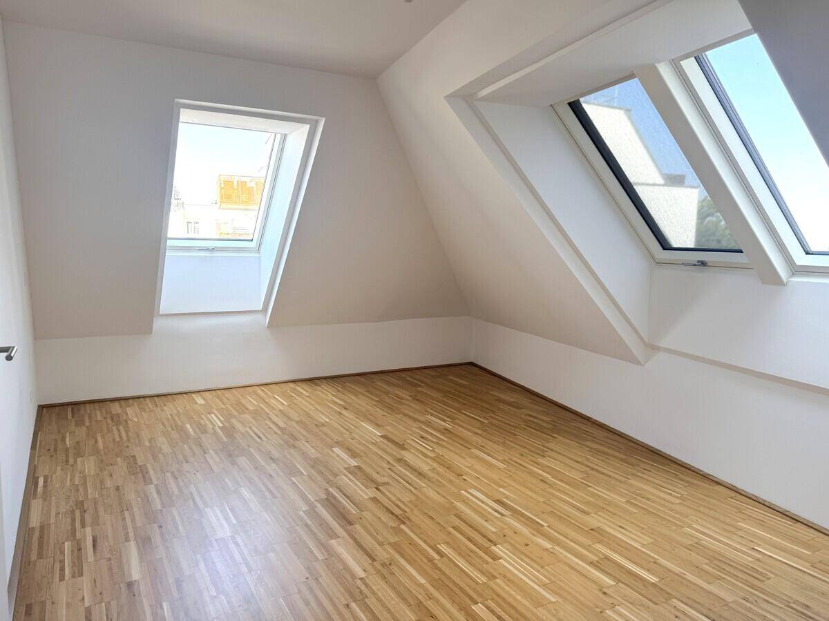 Helles Dachzimmer mit Parkettboden und zwei großen Dachfenstern für viel Tageslicht.