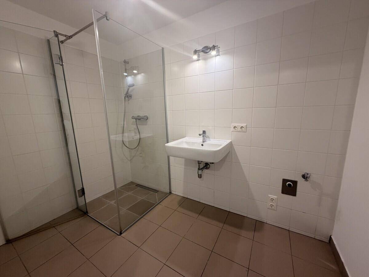 Modernes Badezimmer mit begehbarer Dusche, weißem Waschbecken und Fliesenboden.