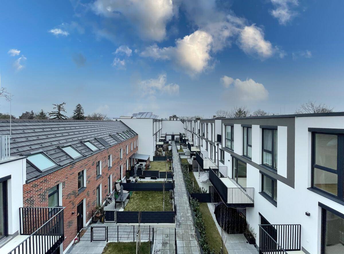 Moderne Wohnanlage mit Reihenhäusern, Gärten und Balkonen unter blauem Himmel.