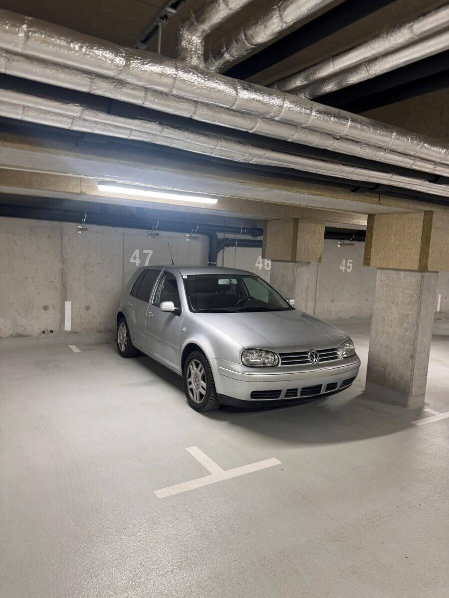 Einzelner Stellplatz in der Tiefgarage mit einem geparkten Auto und sichtbaren Versorgungsleitungen an der Decke.
