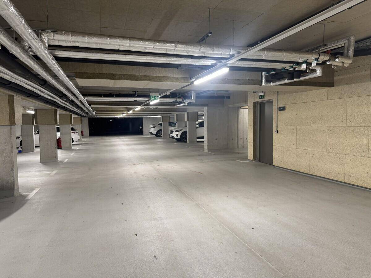 Tiefgarage mit mehreren Stellplätzen und Zugang zum Aufzug, umgeben von Betonwänden und -säulen.