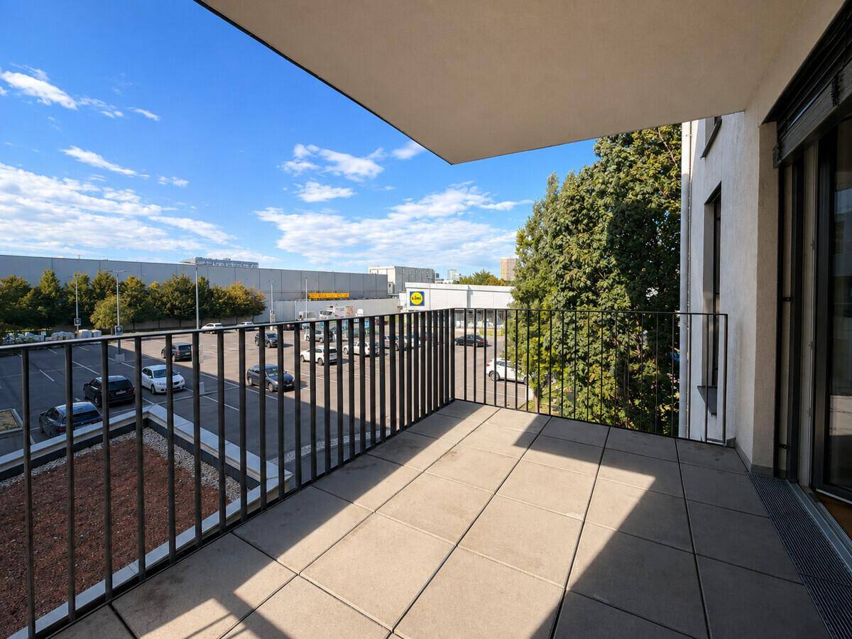 Geräumiger Balkon mit Fliesenboden und Blick auf einen Parkplatz und Bäume.
