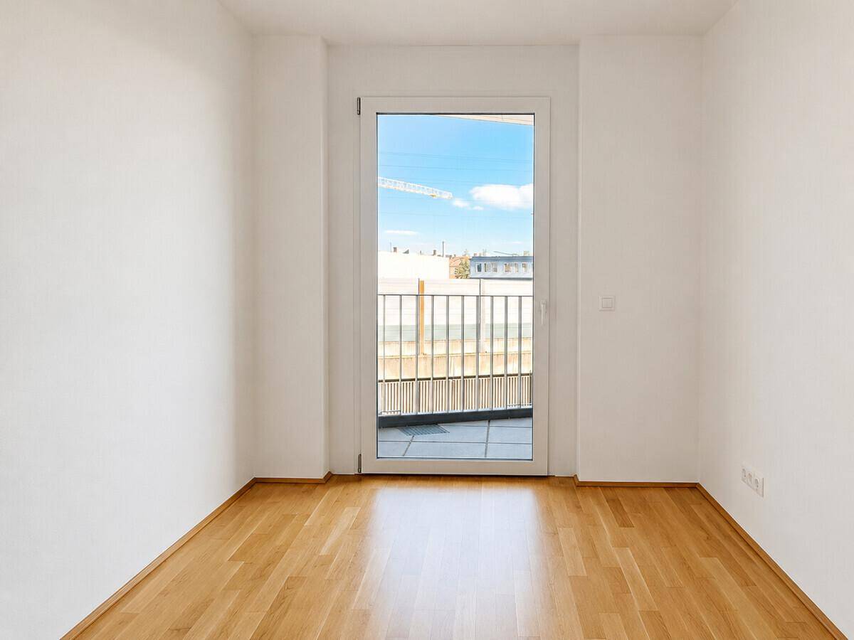 Heller, leerer Raum mit Parkettboden und Zugang zu einem kleinen Balkon.