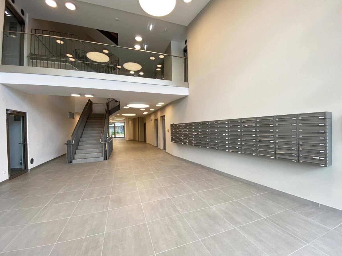 Geräumiger und heller Eingangsbereich eines modernen Gebäudes mit Treppe und Briefkästen.