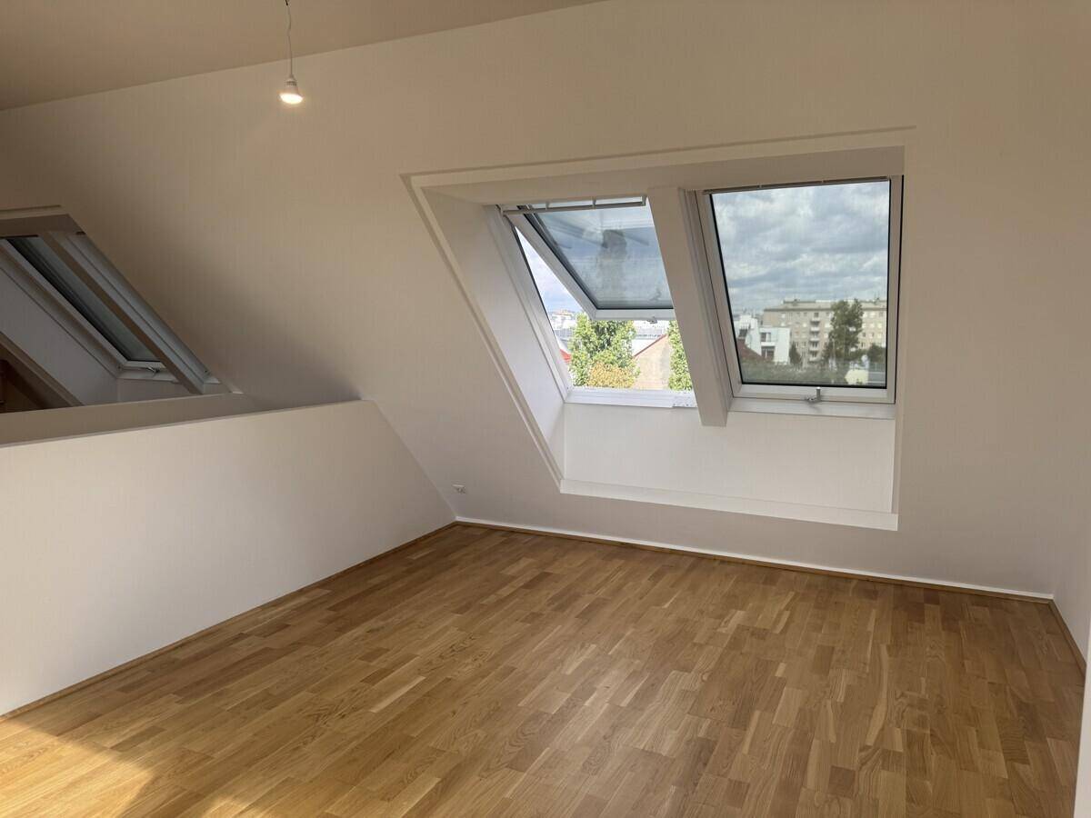 Helles Zimmer im Dachgeschoss mit Holzboden und zwei Dachfenstern.