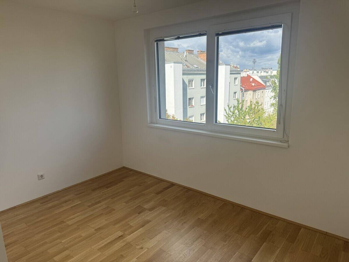 Helles Zimmer mit Holzboden und Blick auf die umliegenden Gebäude der Stadt.