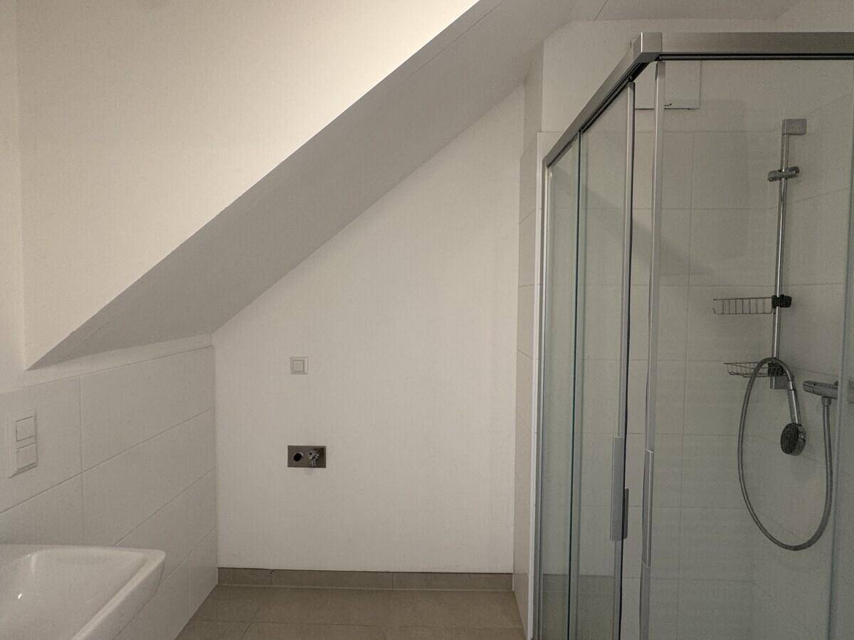 Modernes Badezimmer im Dachgeschoss mit Duschkabine und gefliesten Wänden.