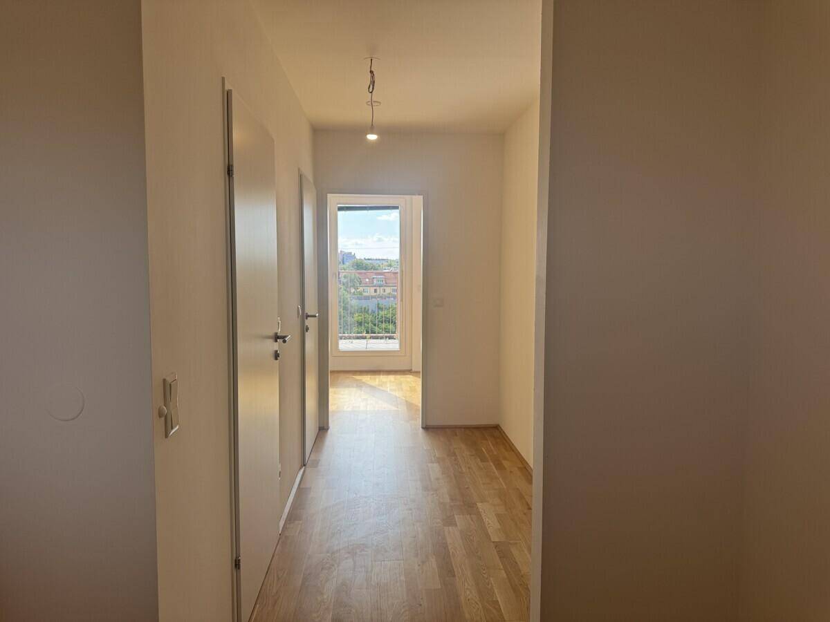 Heller Flur mit Holzboden und Blick auf einen Raum mit Balkonzugang.