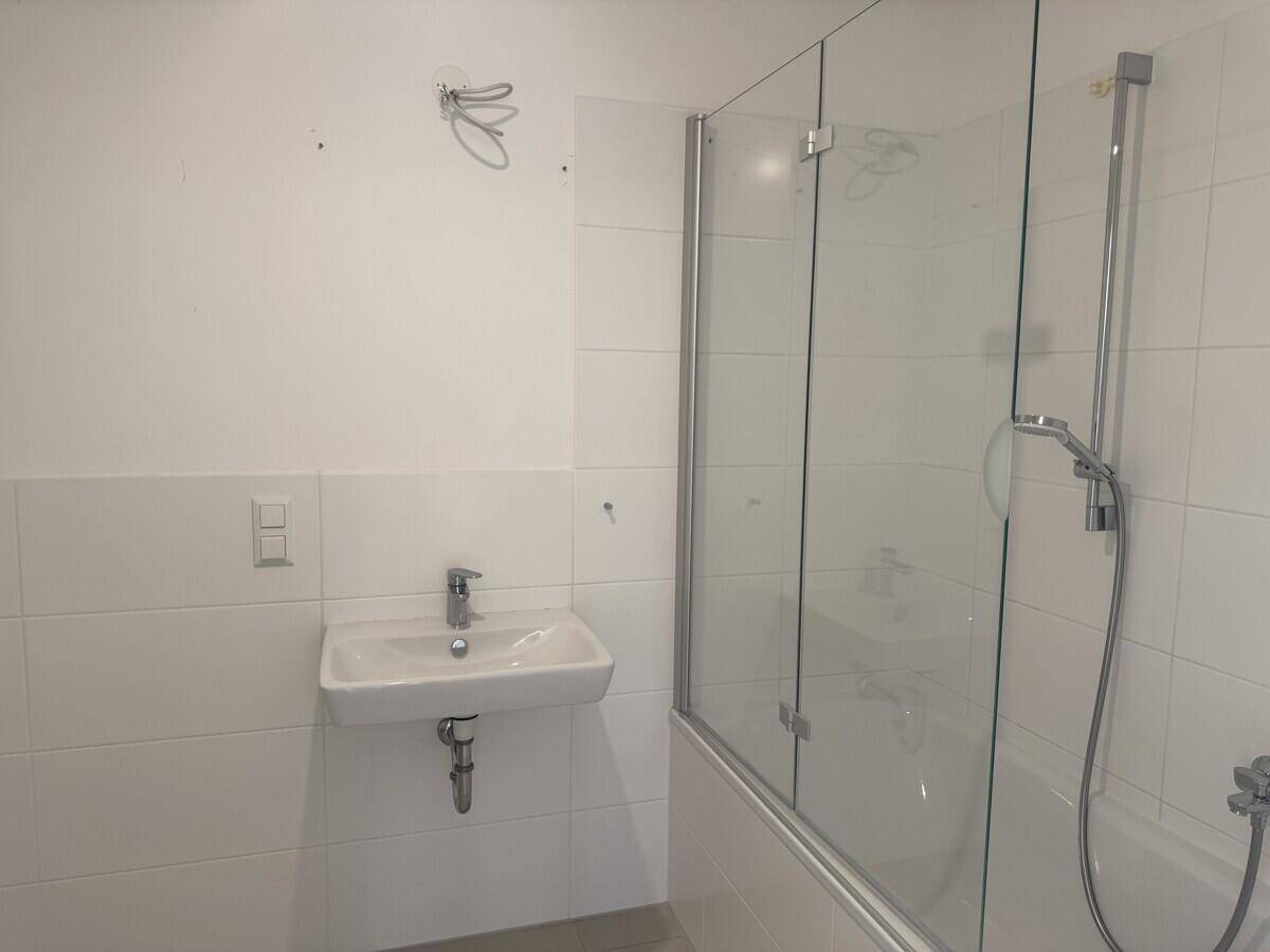 Badezimmer mit Waschbecken, Badewanne mit Duschwand und weißen Fliesen.