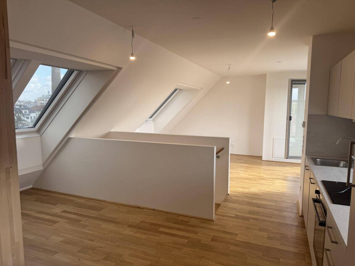 Dachgeschosswohnung mit Holzboden, Dachfenstern und offener Küchenzeile.