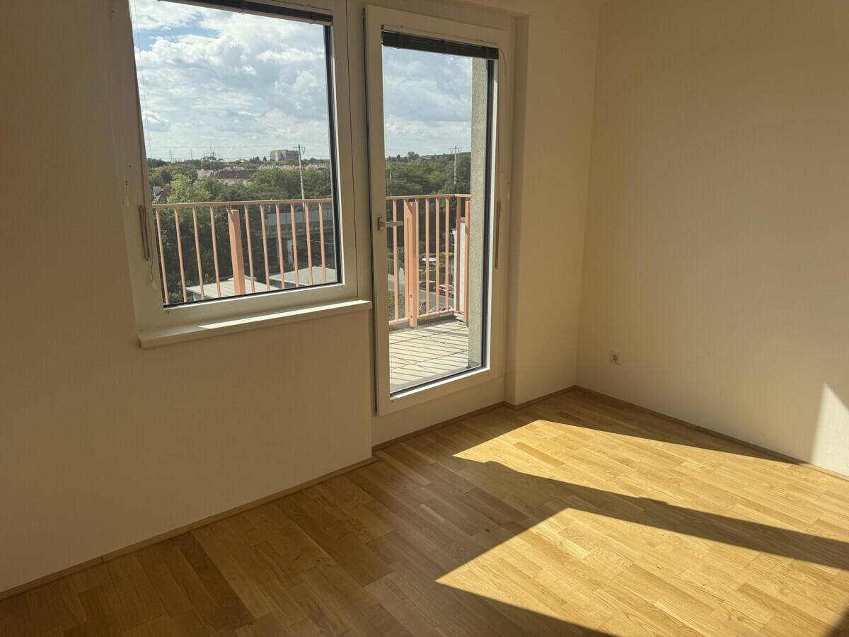Lichtdurchflutetes Zimmer mit Holzboden und Zugang zum Balkon.