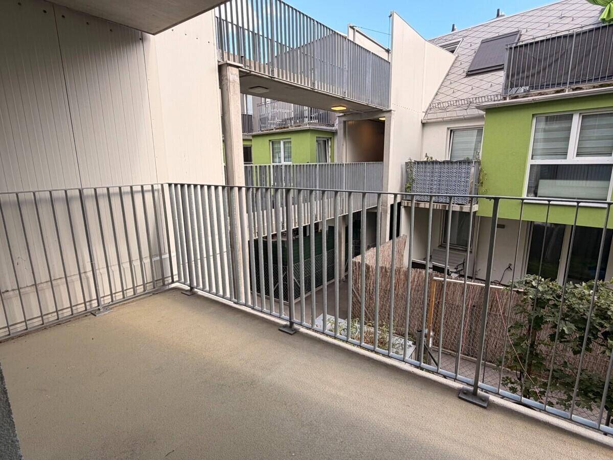 Balkon mit Metallgeländer und Blick auf die Innenhofbebauung mit grünen Fassaden.