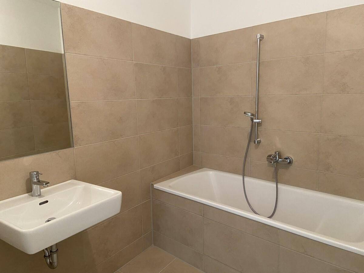 Modernes Badezimmer mit beigefarbenen Fliesen, Badewanne und Waschbecken.