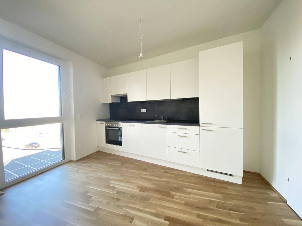 Moderne Einbauküche in Weiß mit dunkler Arbeitsplatte und hellem Parkettboden.