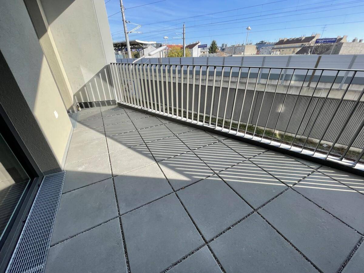 Balkon mit Fliesenboden und Metallgeländer, bietet einen Blick auf die Bahngleise.