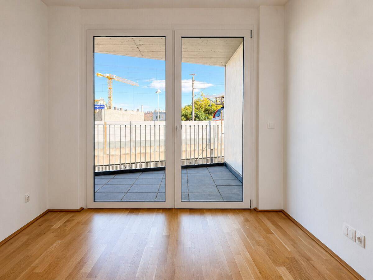 Leerer Raum mit Parkettboden und großem Fenster, das auf einen Balkon führt.