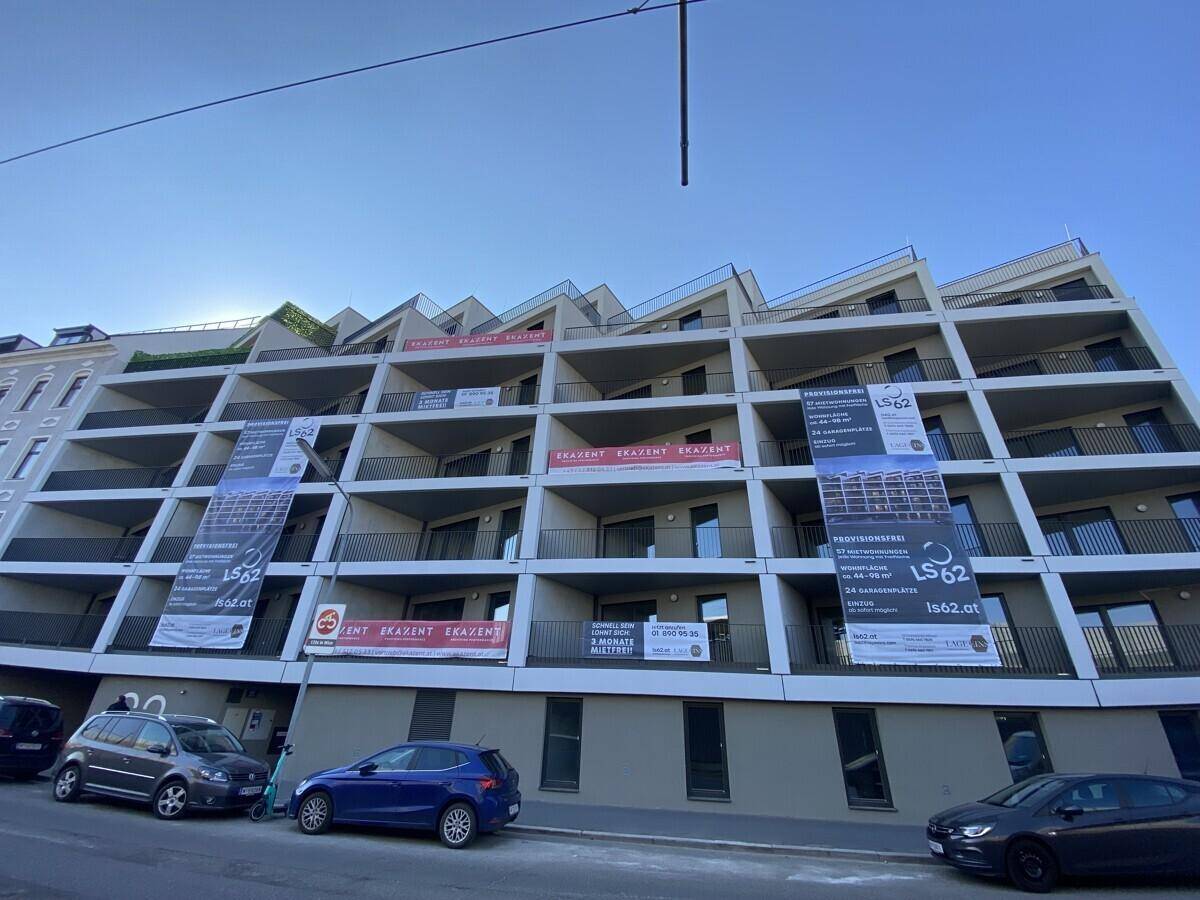 Moderne Wohnhausfassade mit vielen Balkonen und Werbebannern an einem sonnigen Tag.