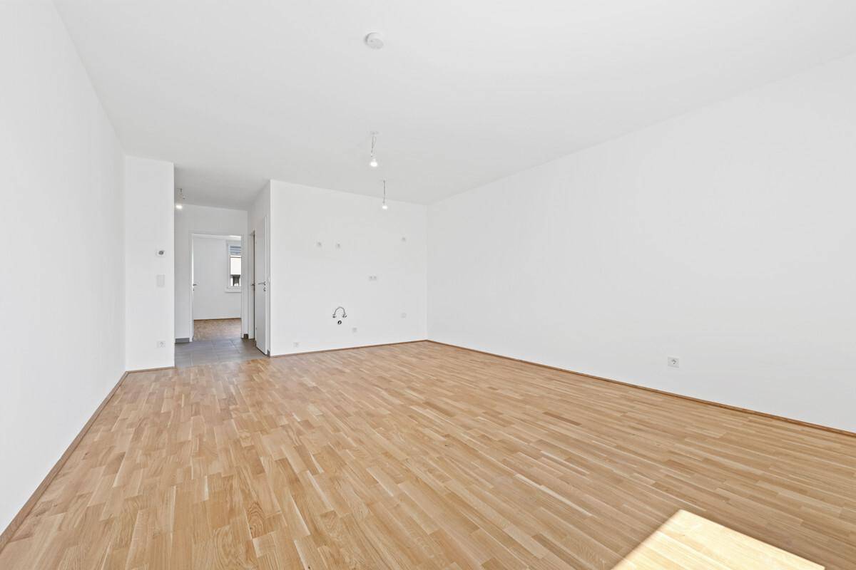 Helles Zimmer mit Parkettboden und weiß gestrichenen Wänden, bietet einen offenen Übergang zum Flur.