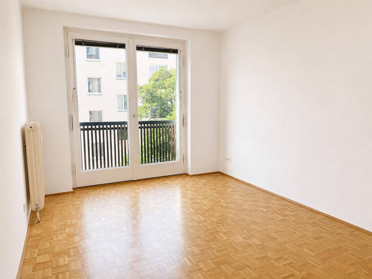 Lichtdurchflutetes Zimmer mit Parkett, Heizkörper und Balkonzugang, bietet einen grünen Ausblick.