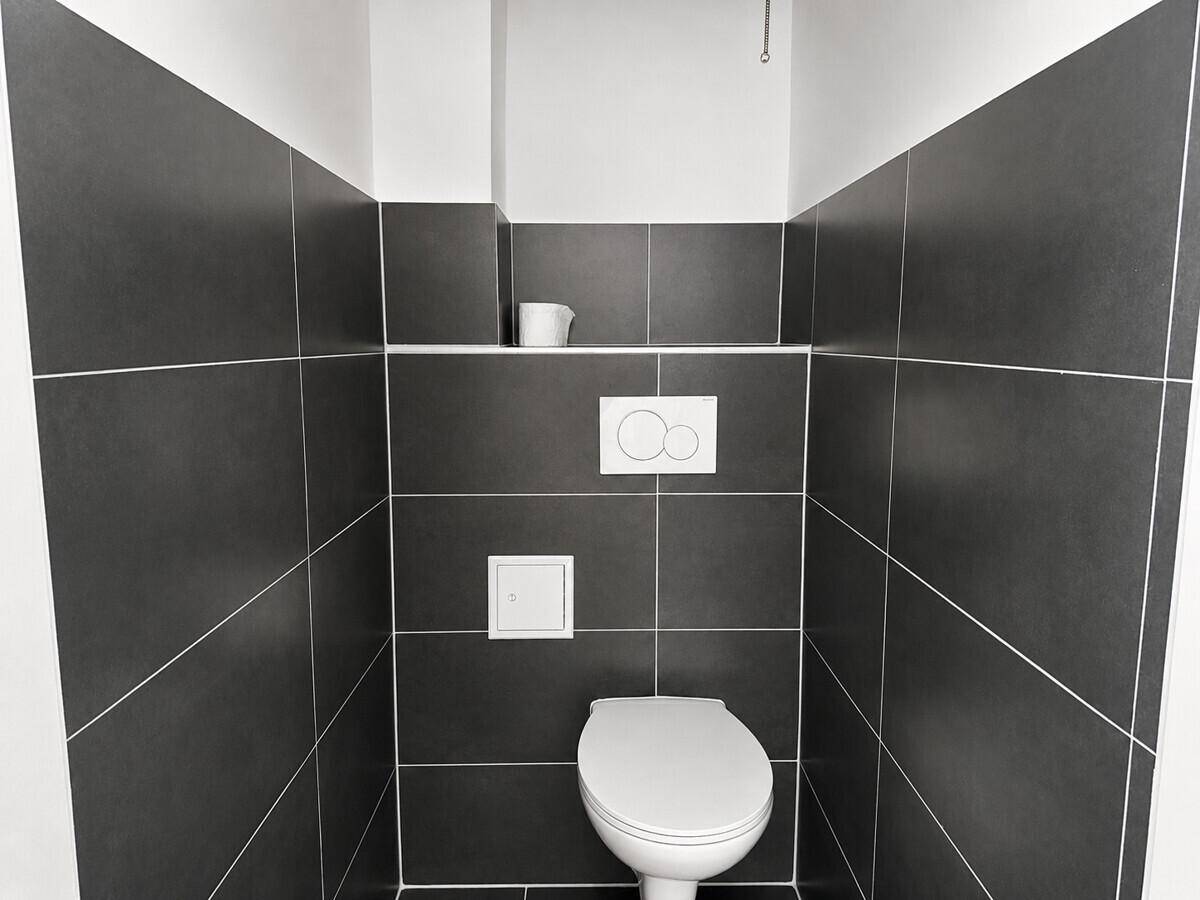 Modernes WC mit dunklen Fliesen und wandhängender Toilette, bietet eine saubere und minimalistische Ästhetik.