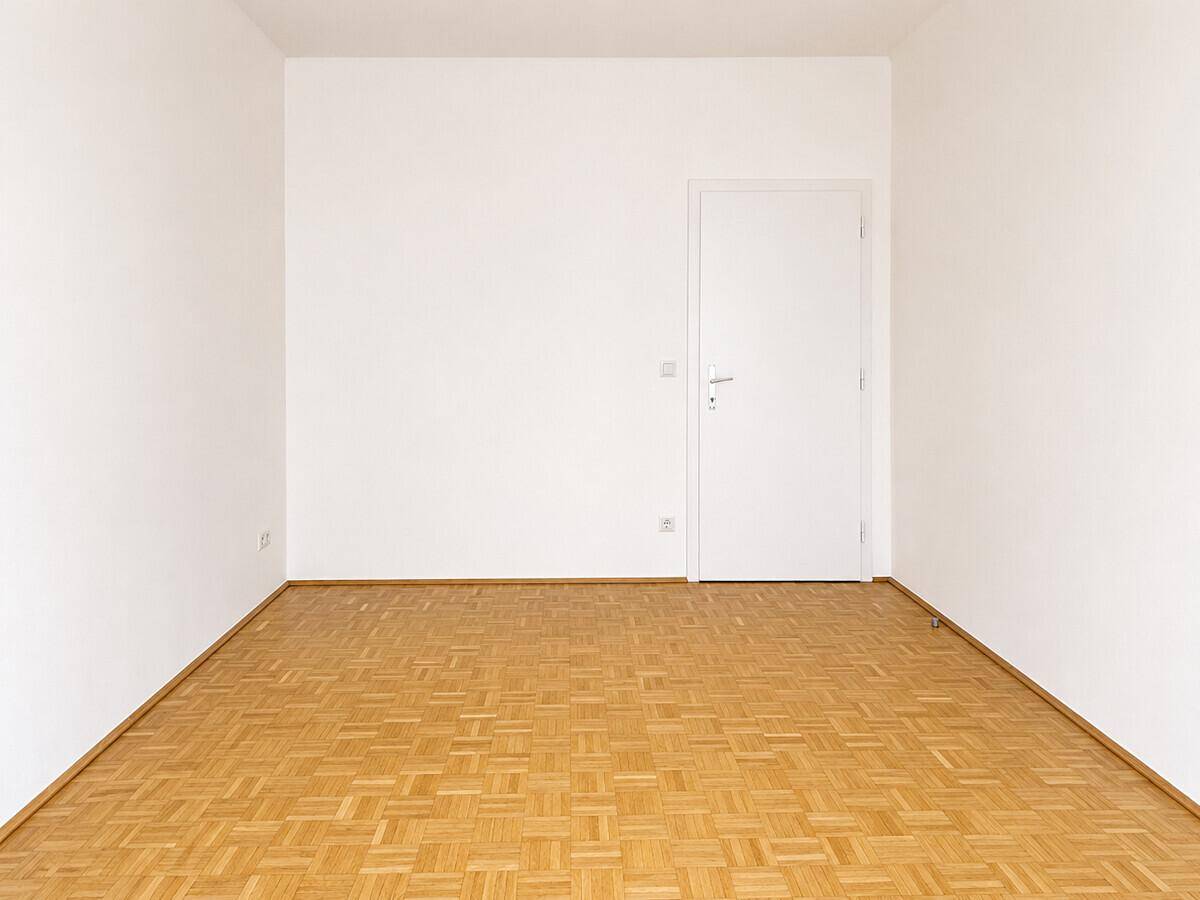 Schlichtes Zimmer mit Parkettboden und weißer Tür, bietet eine neutrale Basis für neue Bewohner.