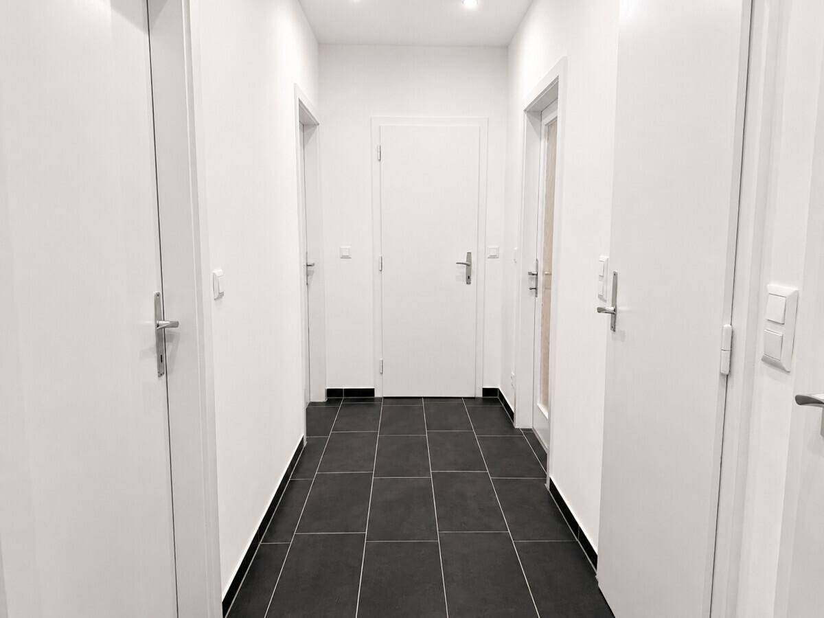 Heller Flur mit dunklem Fliesenboden und mehreren weißen Türen, verbindet die verschiedenen Wohnbereiche.