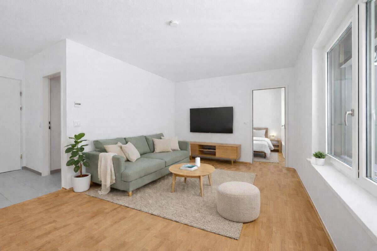 Gemütliches Wohnzimmer mit modernem Sofa, Holzboden und Blick in ein angrenzendes Schlafzimmer.