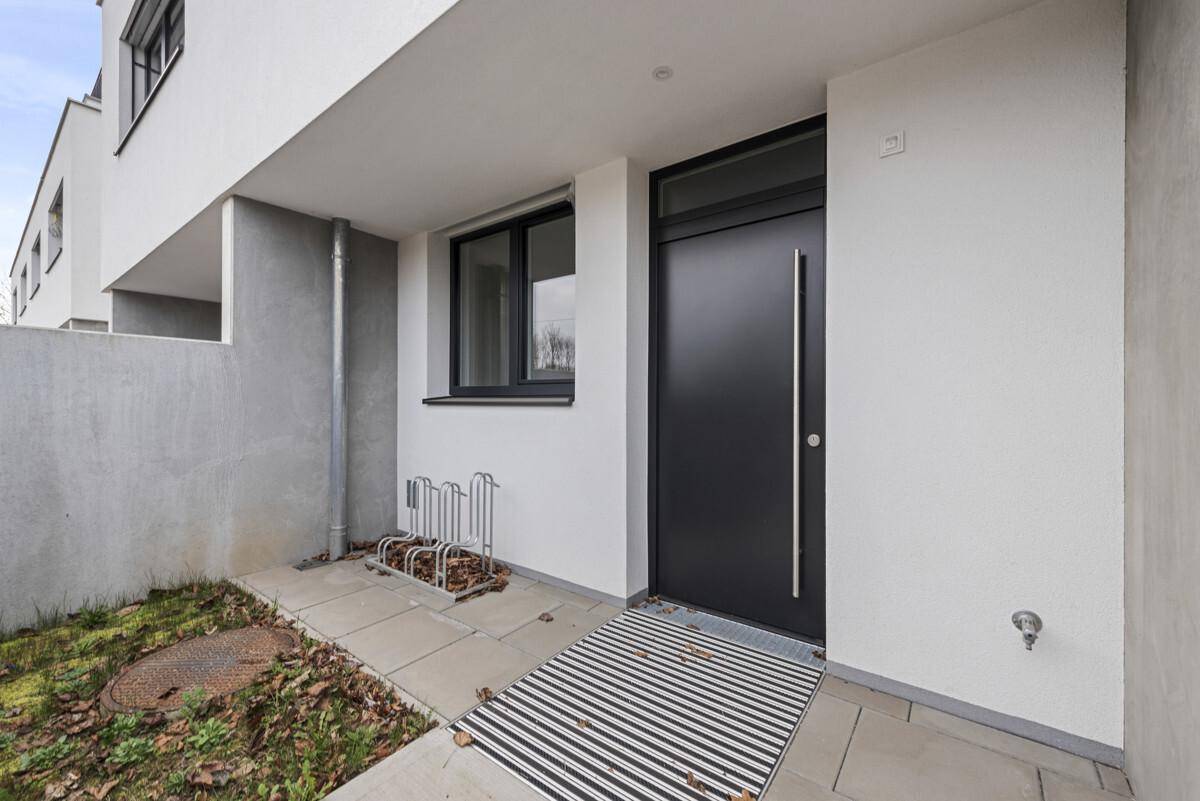 Moderner Eingangsbereich eines Reihenhauses mit dunkler Tür und Fahrradständern.