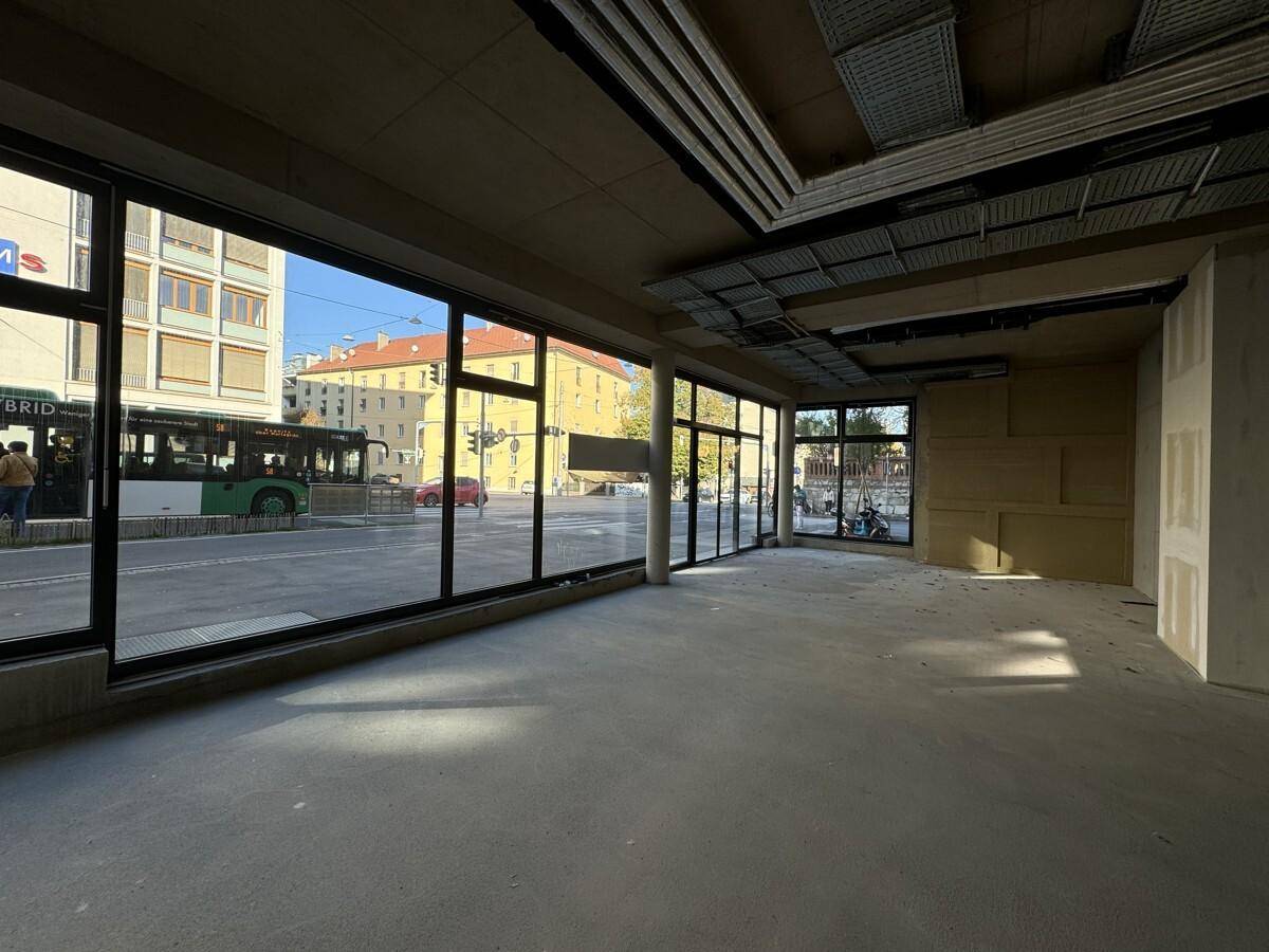 Unfertiger Gewerberaum mit großen Schaufenstern zur Straße und Betonboden, ideal für Einzelhandel oder Büro.