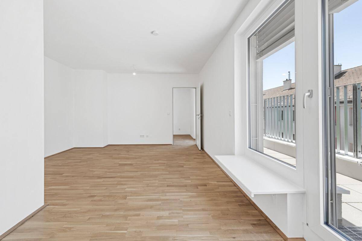 Heller, leerer Raum mit Parkettboden und Zugang zu einem Balkon oder einer Terrasse.