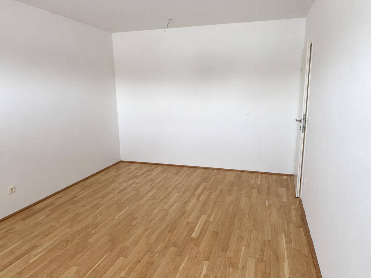 Leeres Zimmer mit hellem Parkettboden und weiß gestrichenen Wänden, bereit zur individuellen Gestaltung.