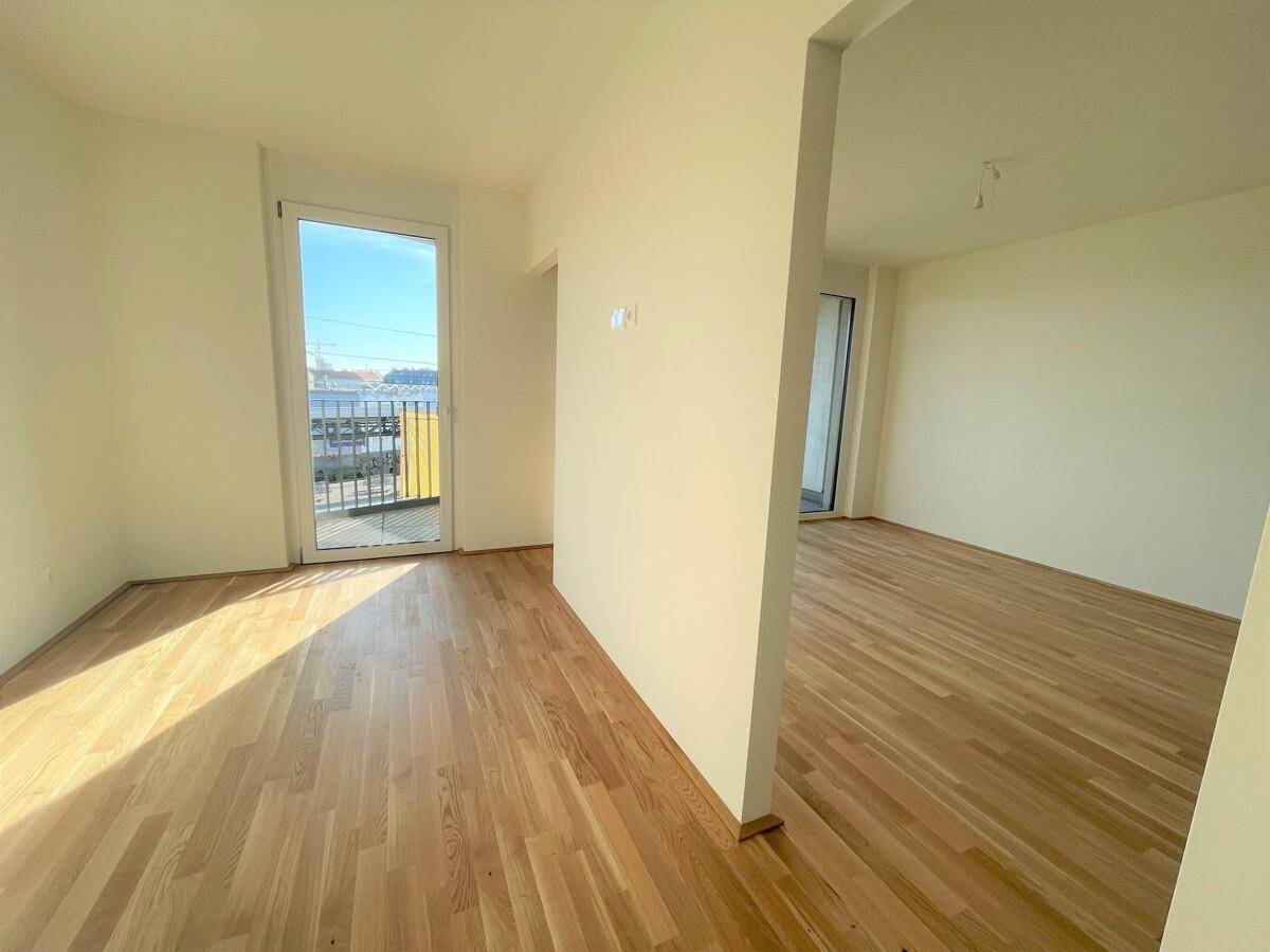 Sonniger Raum mit Parkettboden und Zugang zu einem Balkon, ideal für Wohn- oder Schlafbereich.