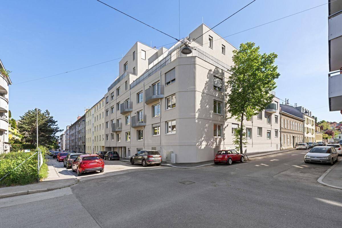 Modernes Wohngebäude an einer städtischen Straße mit parkenden Autos und Bäumen.