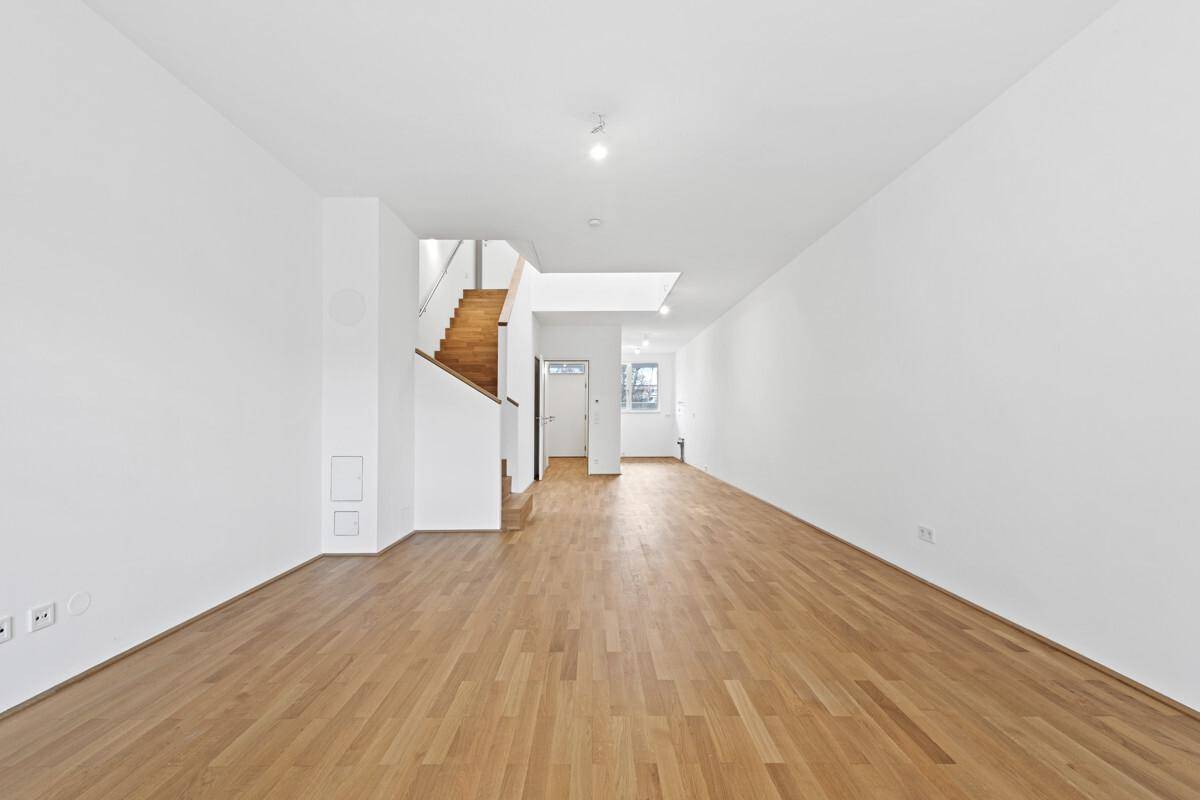 Helles, leeres Wohnzimmer mit neuem Parkettboden und offener Holztreppe zum Obergeschoss.