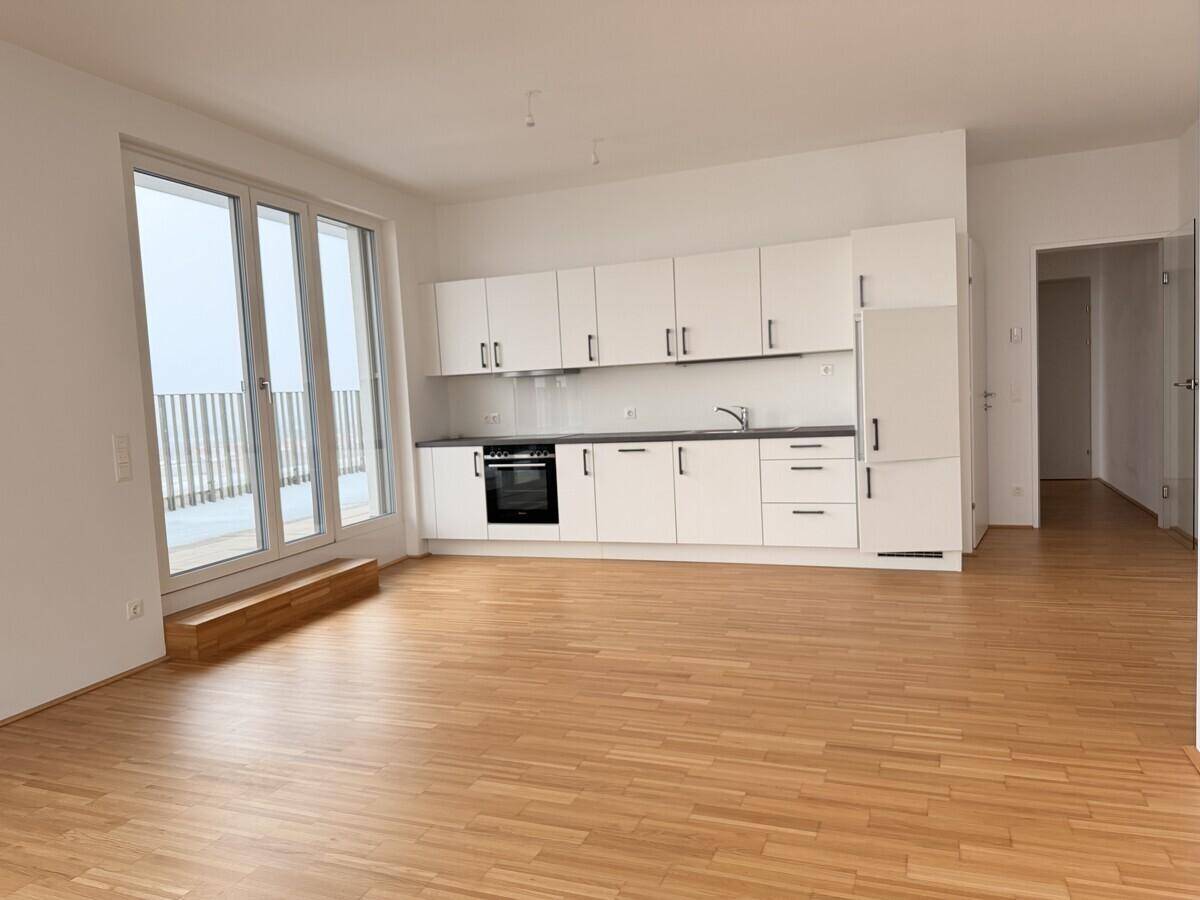 Heller Wohnbereich mit offener Küche, Parkettboden und großen Fenstern mit Zugang zum Balkon.