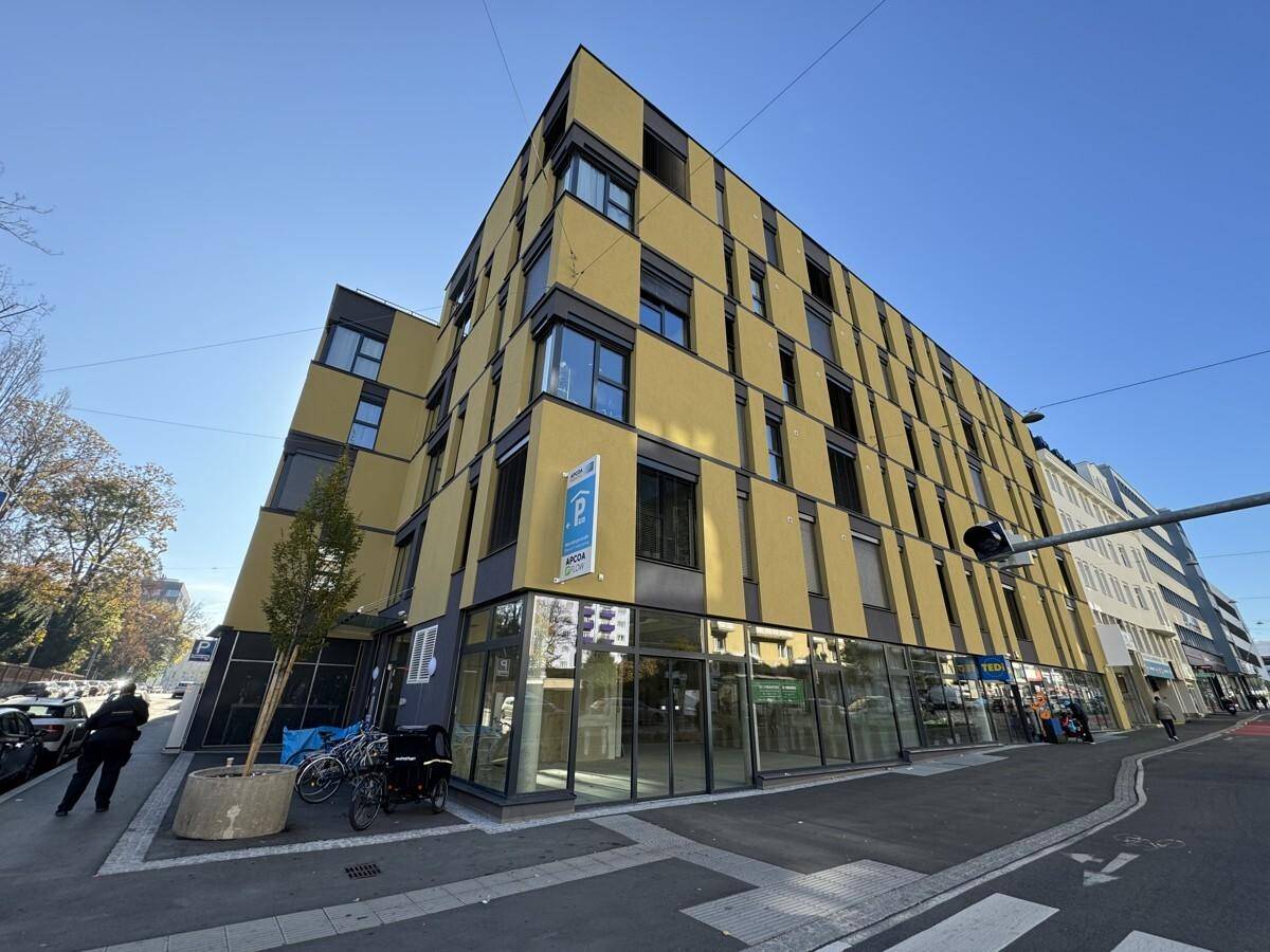 Gesamtansicht des modernen Gebäudes mit gelber Fassade, großen Fenstern und Gewerbeflächen im Erdgeschoss.