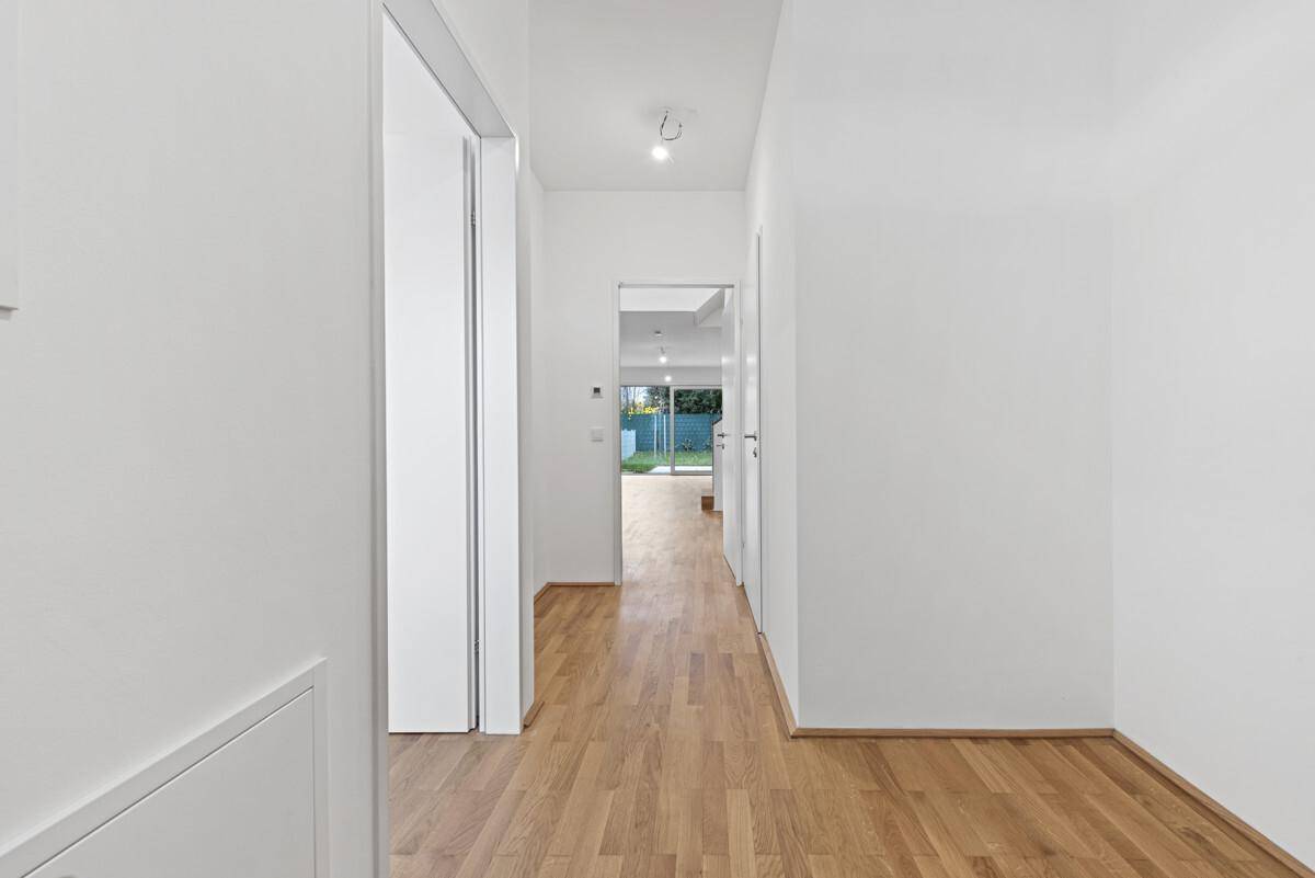 Heller Flur mit Holzparkettboden, weißen Wänden und Zugang zu weiteren Räumen.