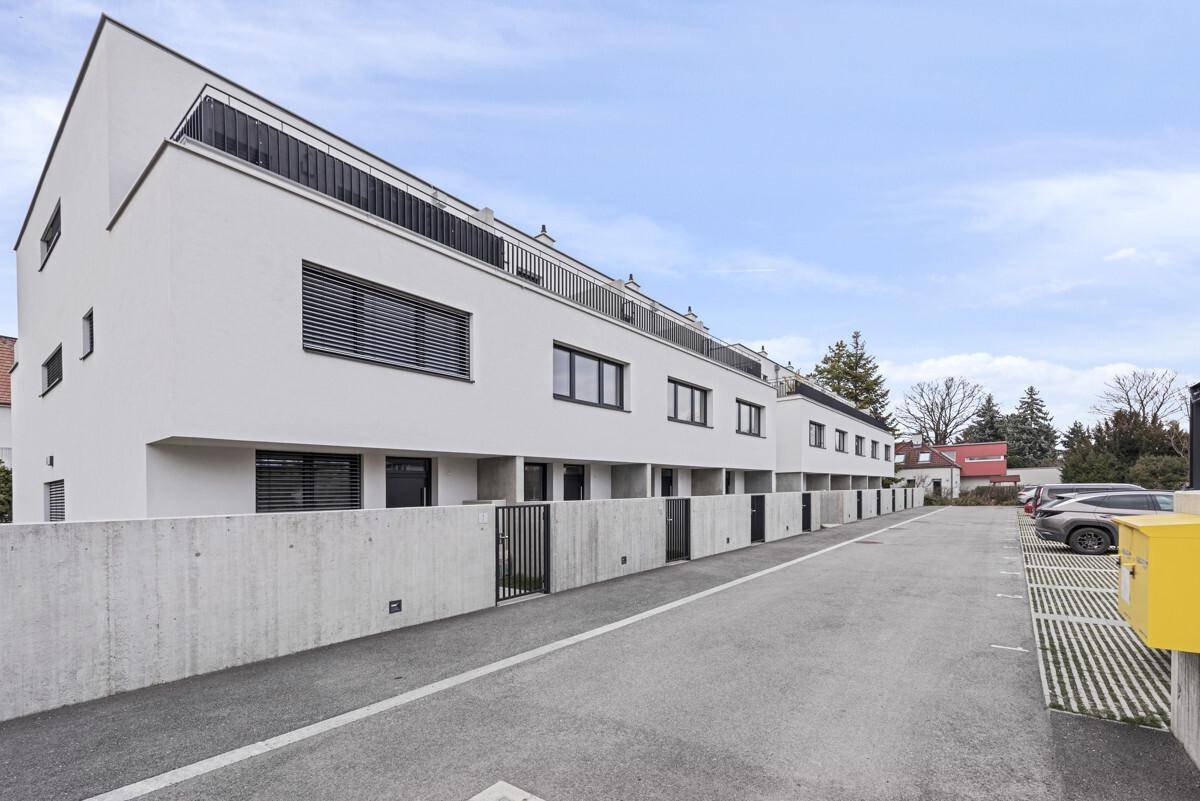 Moderne Reihenhäuser mit weißer Fassade und zugehörigen Parkplätzen entlang der Straße.
