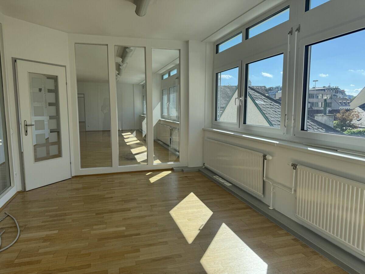 Heller Büroraum mit Parkettboden, Spiegelfronten und Fenstern, die einen Blick über die Dächer der Stadt bieten.