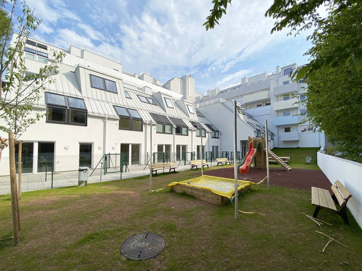 Gemeinschaftlicher Gartenbereich mit Spielplatz, Rutsche, Sandkasten und Bänken hinter dem Gebäude.