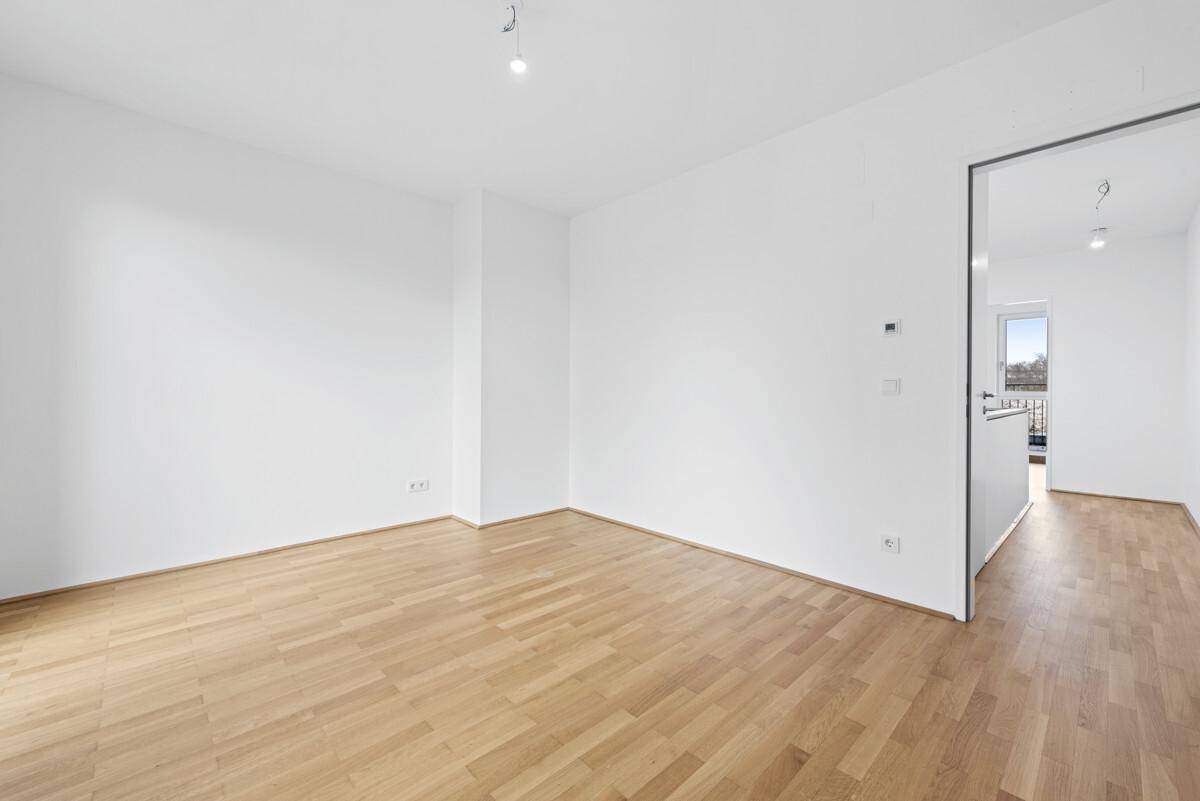 Leeres Zimmer mit Holzparkettboden und Zugang zu einem Balkon.