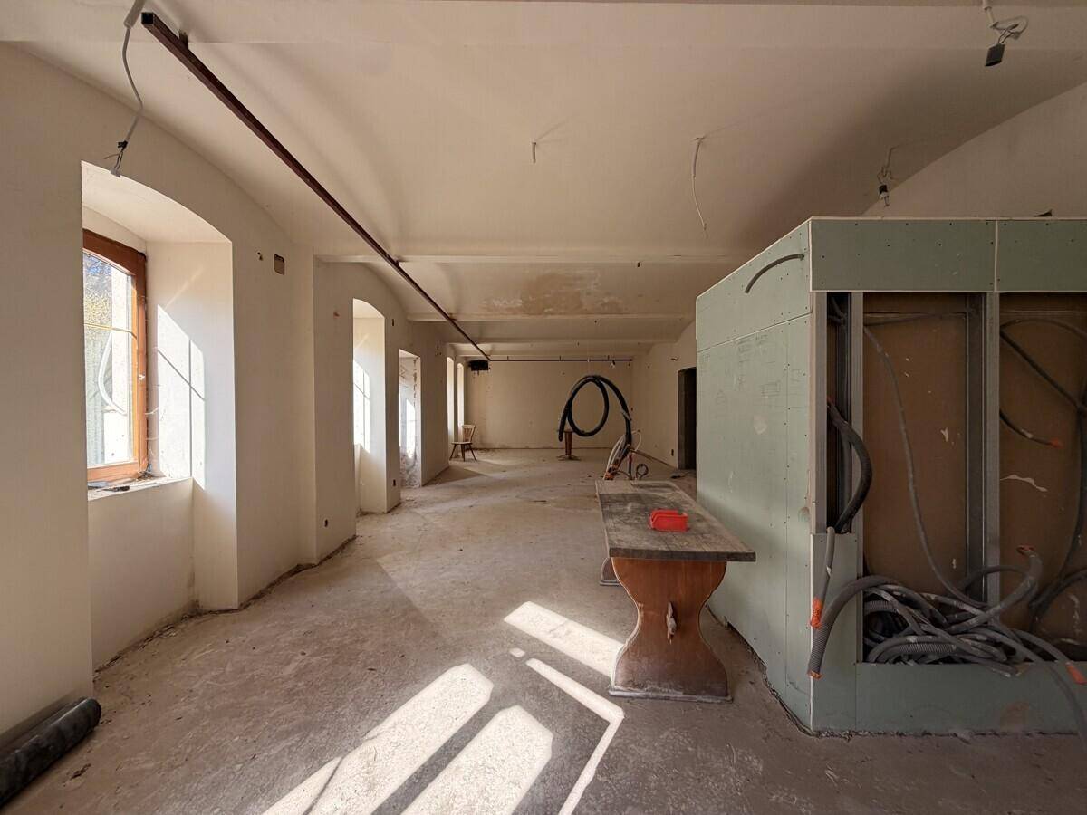 Großer Raum im Rohbau mit hohen, gewölbten Decken, sichtbaren Installationen und viel natürlichem Lichteinfall durch die Fenster.