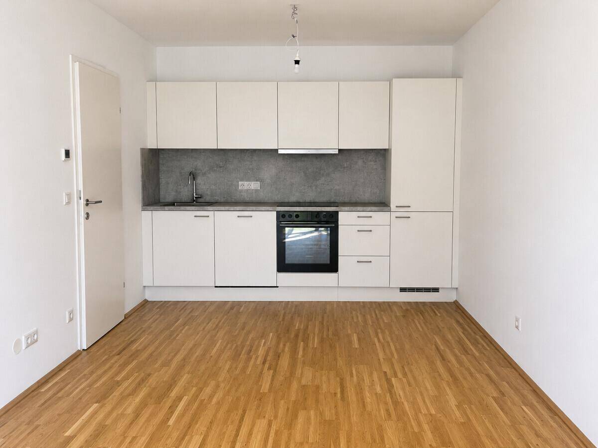 Moderne Einbauküche mit weißen Schränken, integriertem Backofen und Parkettboden in einem hellen Raum.