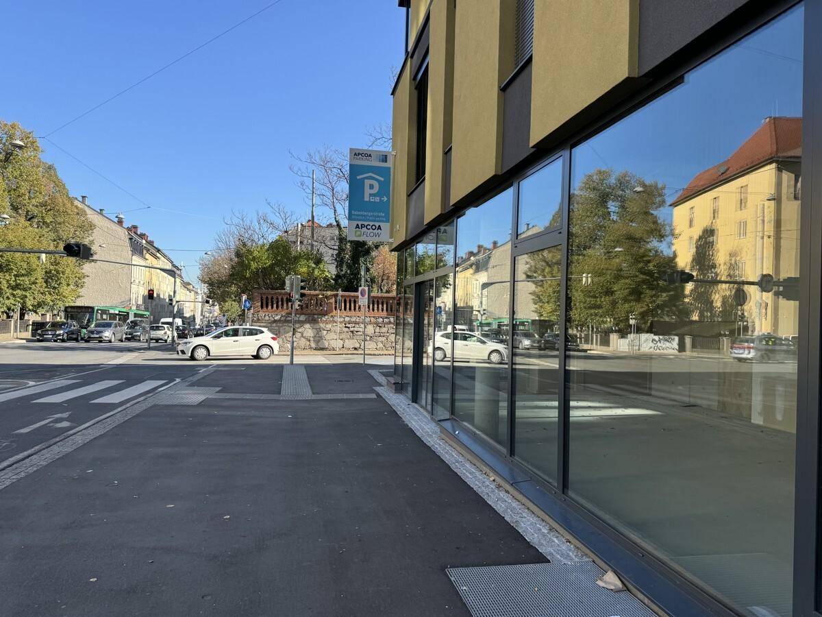 Moderne Gebäudefassade mit großen Glasflächen und Reflexionen der umliegenden Straße und Gebäude.